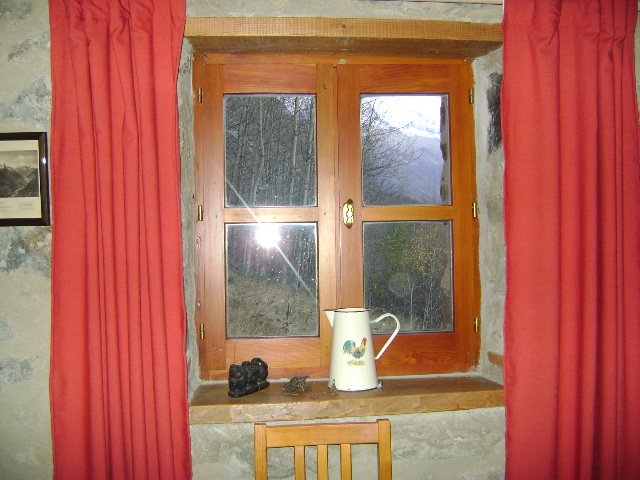 une fenetre de quatre carreaux, avec un cadre en bois et des rideaux rouges, la montagne derrière la vitre et le reflet du flash dans le carreau gauche, du bas